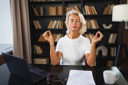 Yoga mindfulness meditation No stress keep calm. Middle aged woman practicing yoga at office. Woman taking break from work meditating relaxing. Mature lady doing breathing practice online yoga at work