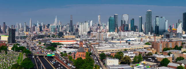 Fototapeta premium Aerial perspective displays traffic on the expressway in Queens leading toward towering skyscrapers of Midtown Manhattan under a clear daytime sky in New York.
