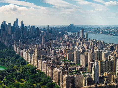 Aerial view of Central Park trees bordering the Upper West Side apartment buildings with the Hudson River and Midtown skyscrapers visible in New York City.