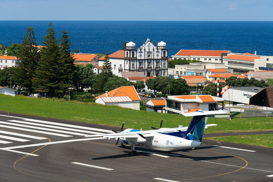 FLORES, PORTUGAL - JULY 20, 2026: A white and blue SATA Air Acores De Havilland Canada Dash 8-200 turboprop airplane on the runway at Flores Airport (FLW), with the town of Santa Cruz das Flores