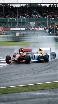 Two open wheel race cars accelerate side by side around a wet circuit. Exposed wheels define both specialized vehicles in the contest. racing competition on a rainy track.