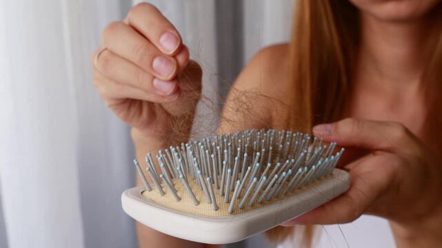 Close-up of woman removing fallen hair from hairbrush showing hair loss and excessive shedding