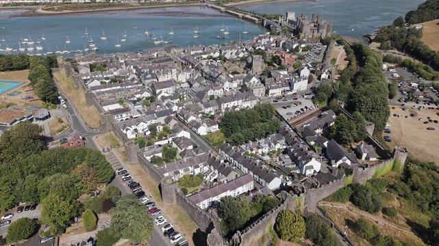 High-angle aerial shot orbiting over medieval city walls toward Conwy Castle, historic fortress and harbor along River Conwy