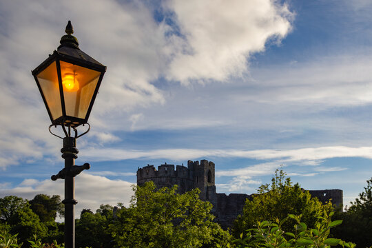 Vintage lit streetlight framing Chepstow Castle ruins against a cloudy sky in Wales