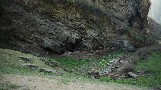 Empty rocky mountain overhang with dry stone riverbed and green slope captured in soft diffused morning light wide shot