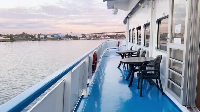 An empty cruise ship deck glides along the Neva River, Saint Petersburg. Tables and chairs rest under a soft sky. The quiet atmosphere brings a peaceful and calm feeling.