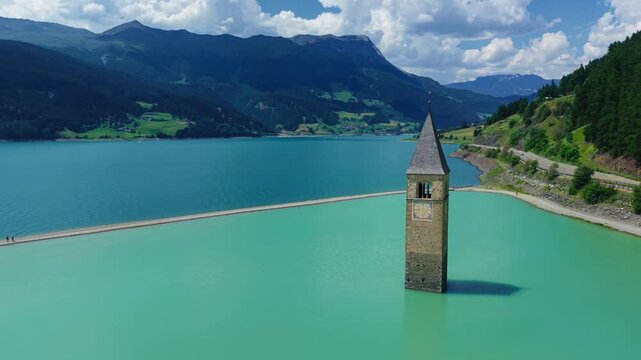 Aerial drone orbital shot circling the historic submerged church bell tower in the turquoise waters of Lake Reschen, South Tyrol, Italy