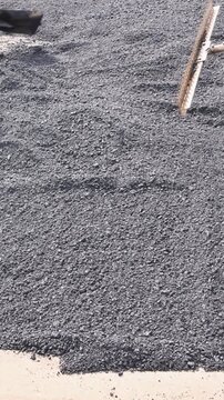 Two workers use shovels to spread asphalt on ground for road project in suburban location