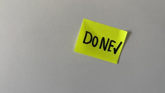 Hand placing done checkmark sticky note on wall