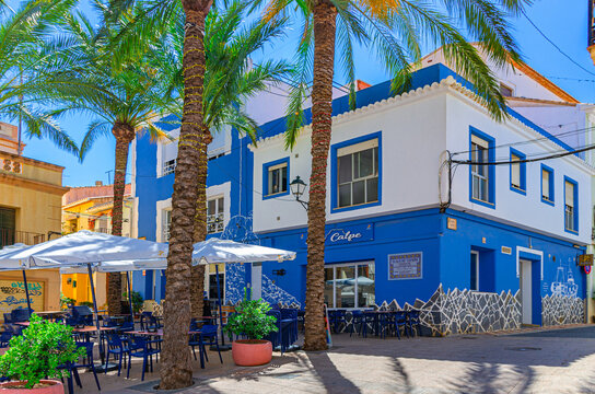 Calpe, Spain, May 30, 2025: Old town Calpe city historical centre with street restaurant outdoor cafe on small square Plaza Espana, typical houses colorful buildings and palm trees in summer day