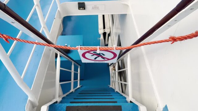 A no entry sign blocks stairs on a cruise ship deck. The red rope creates a clear barrier. The quiet setting brings a cautious and calm feeling.
