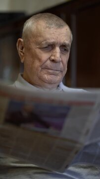 Retired elderly man reading a newspaper indoors, representing aging, leisure, news and everyday life.
