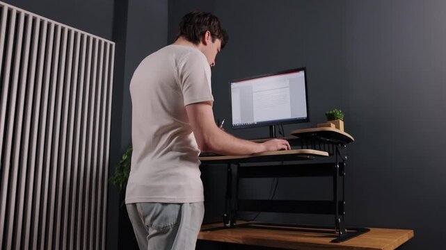 Data entry, white desk, computer standing. From behind, you can see man in white shirt typing on computer at standing desk, with document on screen.