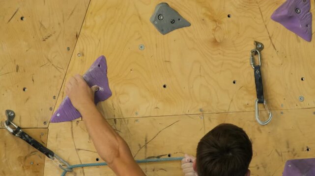 Avid climber tackles climbing apparatus grasping fabricated nooks. Sport enthusiast navigates bouldering wall slow motion