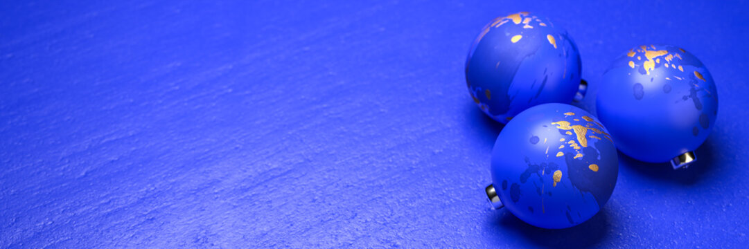 Blue Christmas baubles with golden splatters on a blue stone background. Web banner format with copy space.