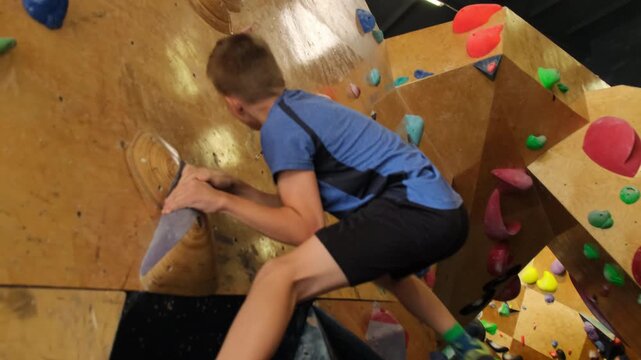 Schoolboy unsuccessfully tries to grab onto stone in sports complex. Young athlete lacks strength and dexterity to climb slow motion