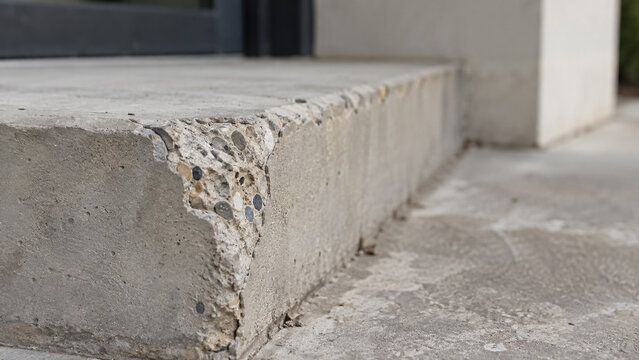 Damaged concrete step with chipped corner exposing coarse aggregate texture. Concept of broken curb, cement damage, outdoor stairs. Copy space.