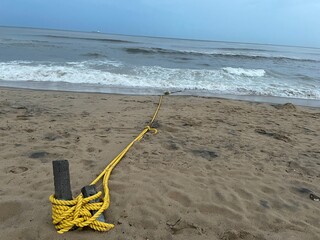 Yellow rope tied to wooden posts on the beach and Scenic Vizag Rushikonda Beach Coastline Landscape Shot During Cloudy and Rainy Weather in the Evening at Rushikonda, Visakhapatnam © AI Digital Art