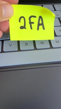 Hand holding two factor authentication note over keyboard