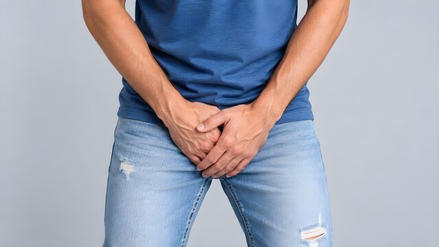 A young man holds his crotch experiencing sudden pelvic pain, discomfort, or an urgent need to use the restroom on a light background