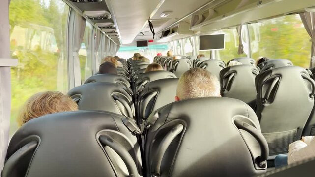 Passengers sit in comfortable seats as a bus travels through Karelia. A person holds a smartphone in the quiet aisle. The orderly ride brings a calm and relaxed feeling.