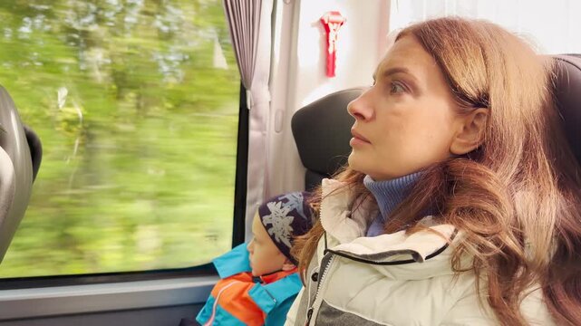 A woman looks forward attentively as a bus travels through Karelia with a young child. Green trees blur past the window. The quiet journey creates a thoughtful and peaceful feeling.