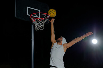 A man performs a slam dunk on a basketball court at night under the glare of bright outdoor lights © nazariykarkhut