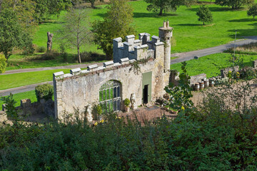 Fototapeta premium A small, weathered stone castle folly featuring a modern window and crenellated tower, nestled within a lush green park landscape - Gwrych Castle, Abergele, Wales, UK