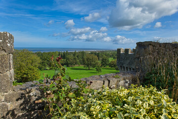 A sunny view from castle battlements overlooks green grounds, distant trees, and the sea under a blue sky with clouds - Gwrych Castle, Abergele, Wales, UK © Robert