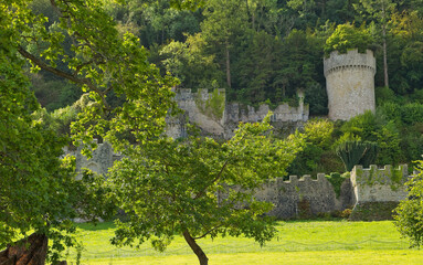 A picturesque landscape features vibrant green trees in the foreground, with ancient castle ruins, stone walls - Gwrych Castle, Abergele, Wales, UK © Robert