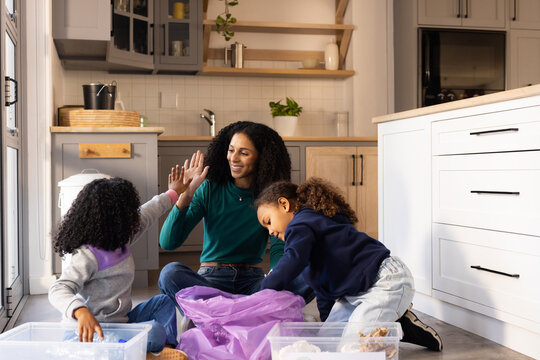 African American mother and girls high-fiving, sorting bins and purple bag on kitchen floor