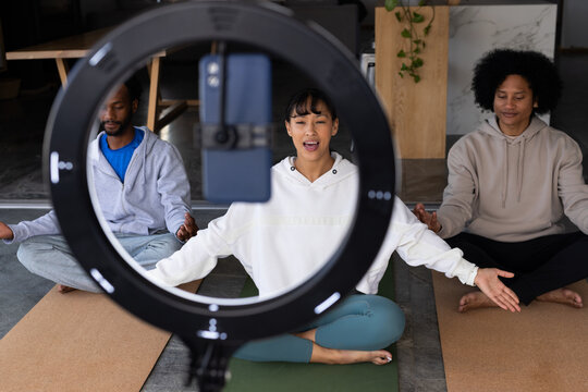 Diverse adults recording yoga session on yoga mats in studio in hoodies with ring light phone