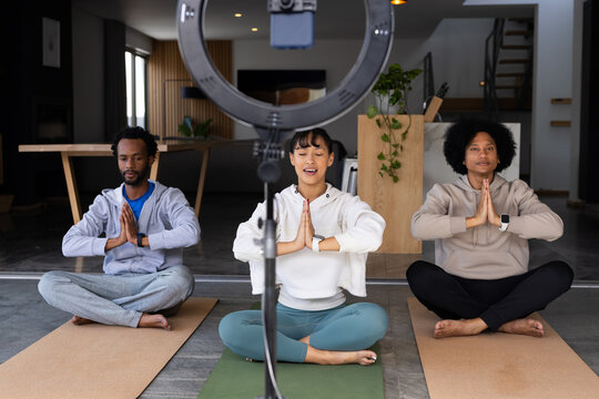 African American friends sitting cross legged on yoga mats at home, recording with ring light