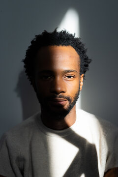African American man posing with ribbed sweater against smooth gray wall with light bisecting face