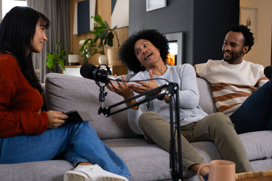 African American hosts recording conversation on gray sofa in room with microphones