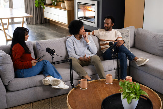 African American friends recording podcast on grey sofa in living room with microphones, tablet