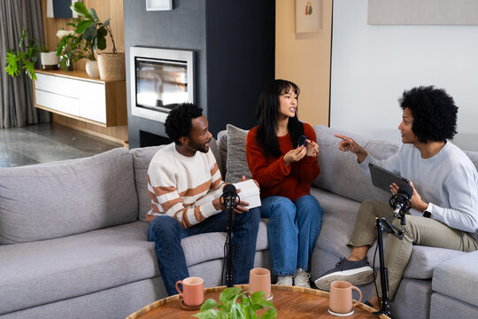 Diverse friends holding tablet and gadget while recording on sectional sofa with microphones