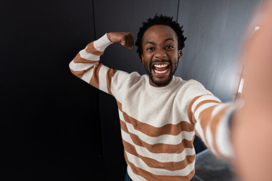 Adult man smiling while flexing left arm and holding smartphone at studio with striped sweater