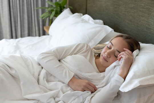 Adult female lying on right side of bed in bedroom, wearing sleepwear, holding white pillow