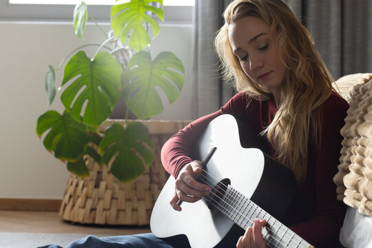 Adult woman sitting on living room floor holding black guitar pick visible wearing maroon top