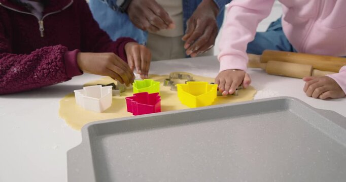 Adult placing tray on kitchen counter is starting hands pressing cutters into rolled dough to bake