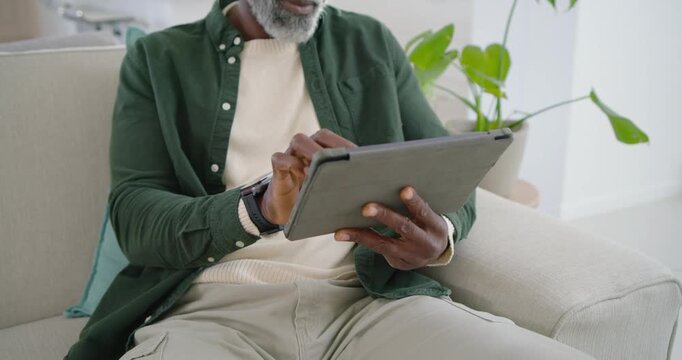 Steadying tablet with left hand, man is tapping and swiping screen to browse content on sofa