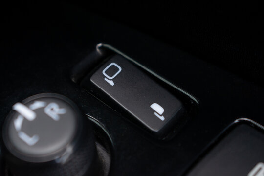 Close-up macro shot of car power folding side mirror switch button on door panel.