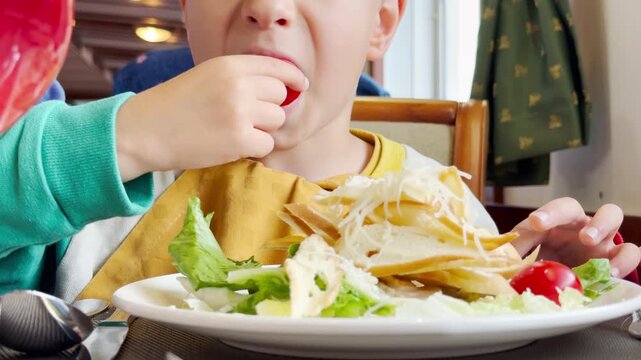 A young child eats a fresh salad on a cruise ship. He feels happy and hungry during the meal. The cozy dining room creates a joyful atmosphere.