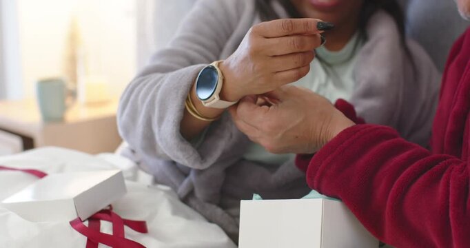 Senior couple opening gift, man helping woman fastening smartwatch with white band on bed