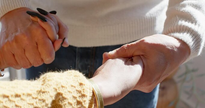 White-sweater hand is holding wrist and stretching yellow-sleeve hand with black nails near window