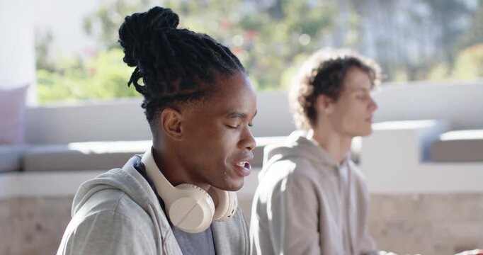 Diverse male friends sitting on patio following guided audio with headphones and holding Gyan mudra