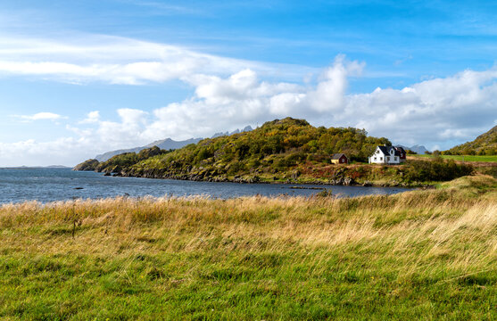 Autumn coastal landscape near Mortsund in the Lofoten Islands with blue sea, rocky islands, rugged mountains and a cloudy blue sky.