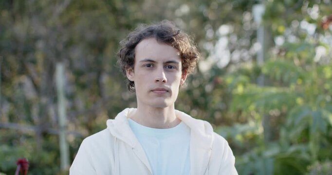 Man in twenties wearing hoodie, blue tee, standing in garden, sunlight coaxing smile, red pot left