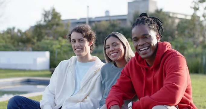 Diverse friends responding to camera, smiling and leaning on bench by pool, red hoodie visible